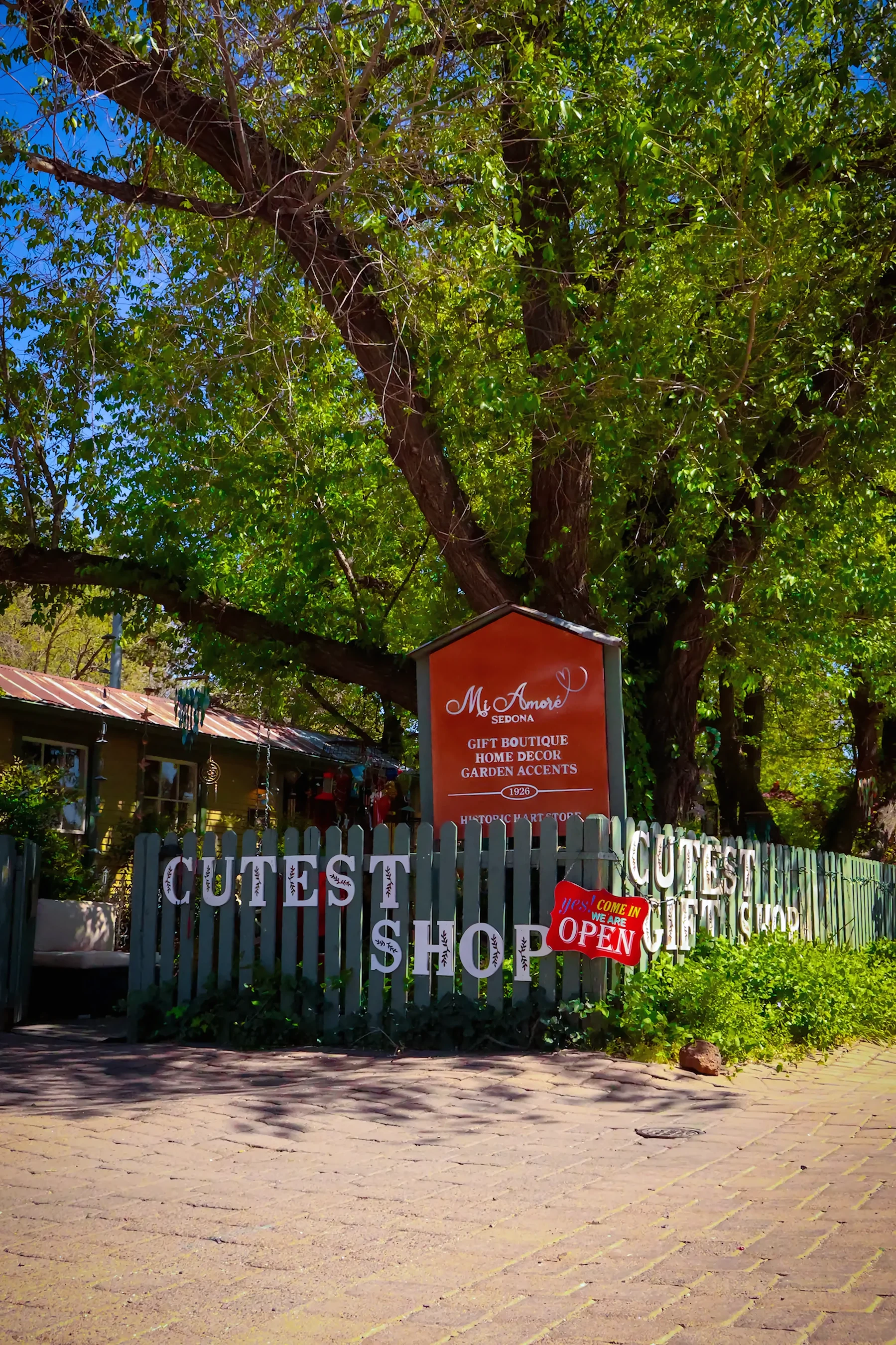 Mi Amoré Sedona’s garden gate and orange shop sign beneath a leafy tree at the Hart Store